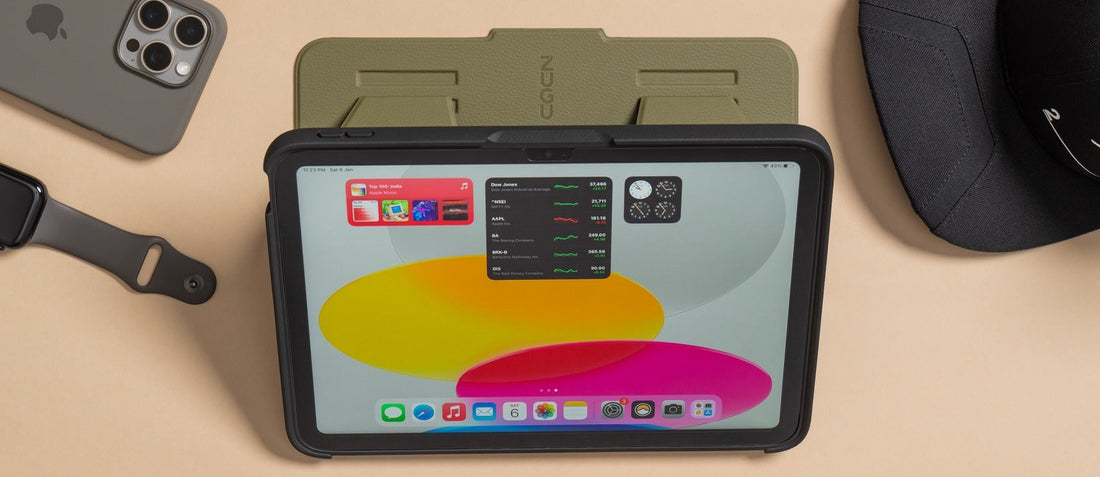 An iPad, surrounded by multiple accessories, like SD cards, Apple Watch, iPhone, headphones, and a clock