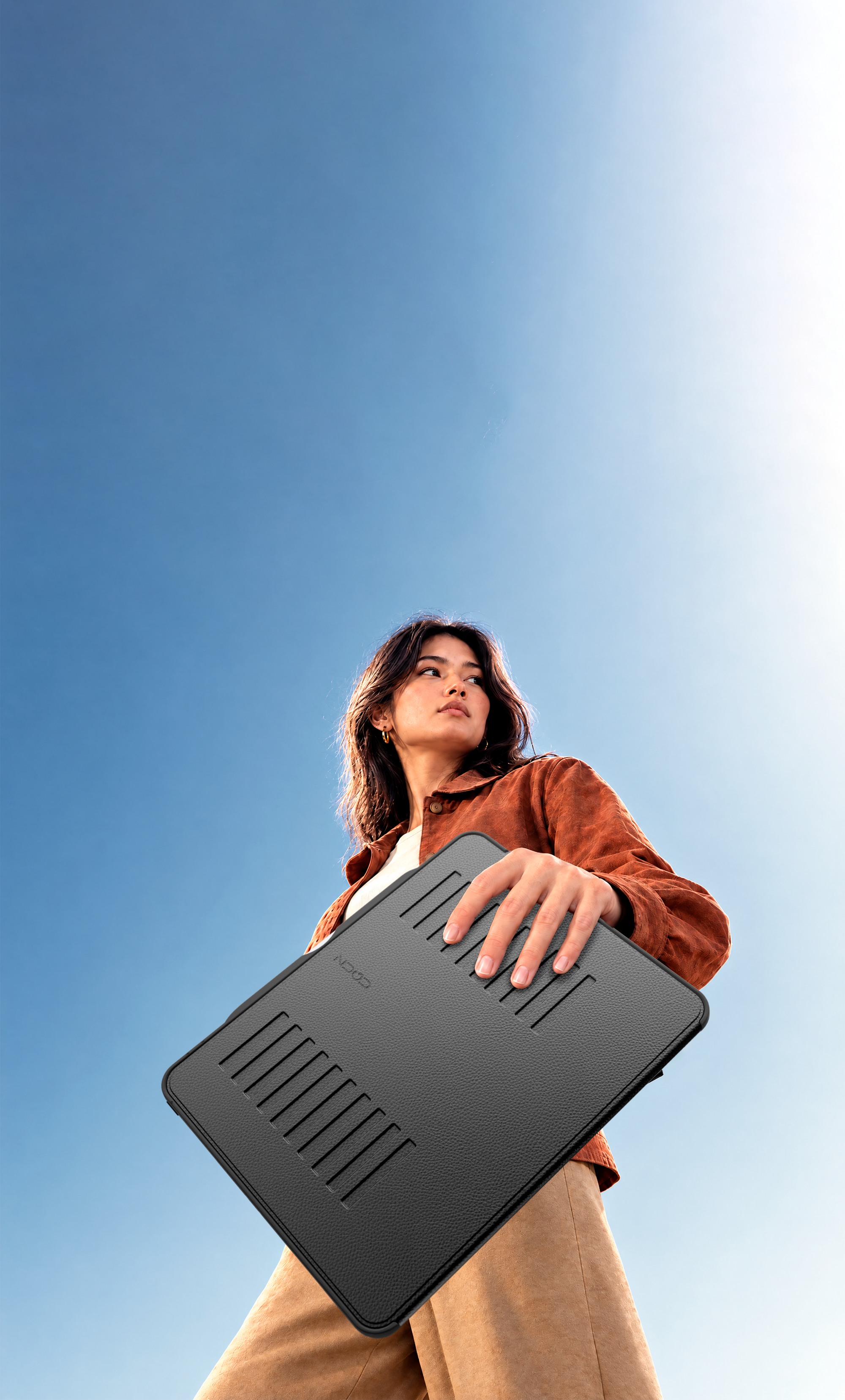 Low angle image of a woman holding the Light Series case while walking with the sky behind her.