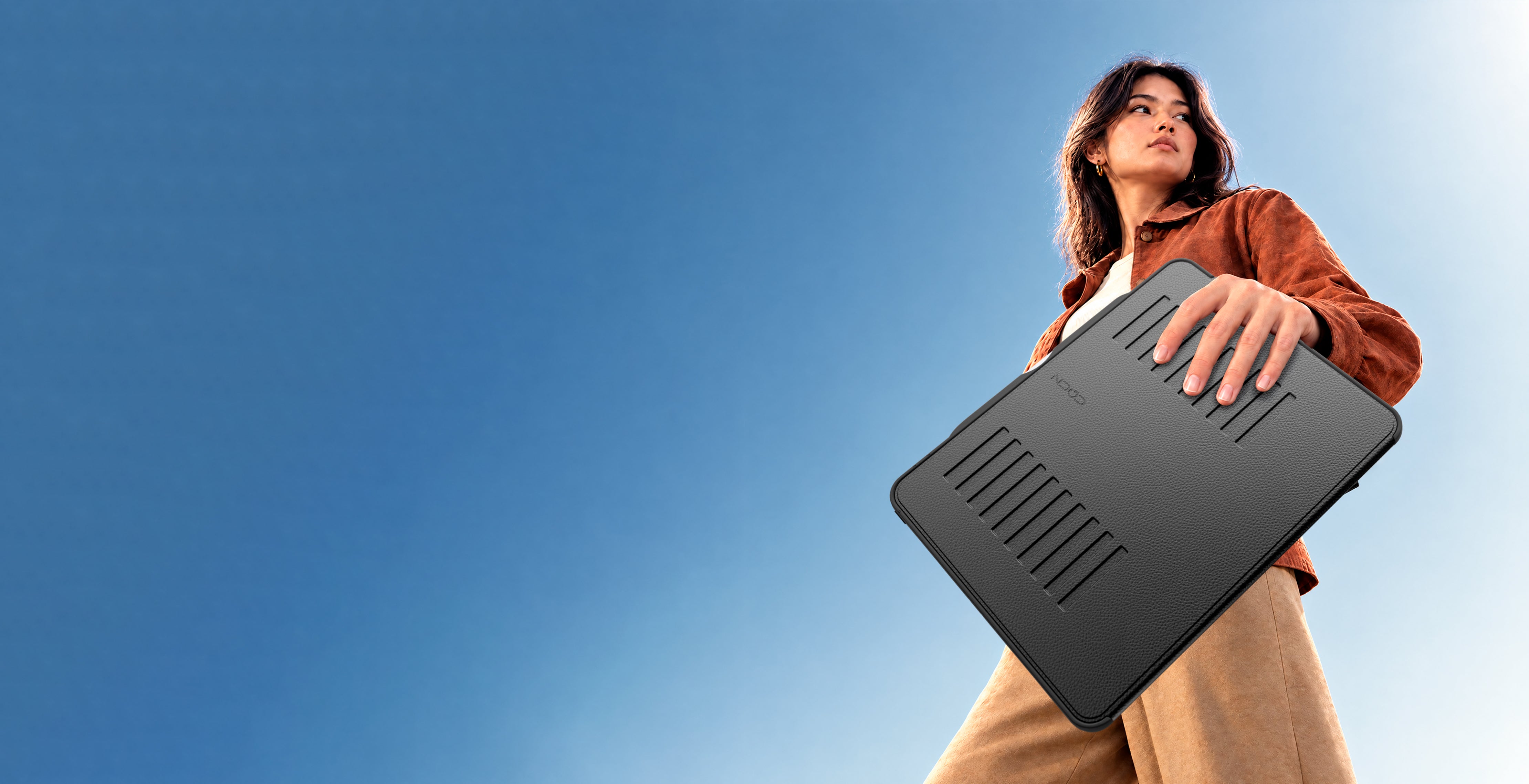 Low angle image of a woman holding the Light Series case while walking with the sky behind her.